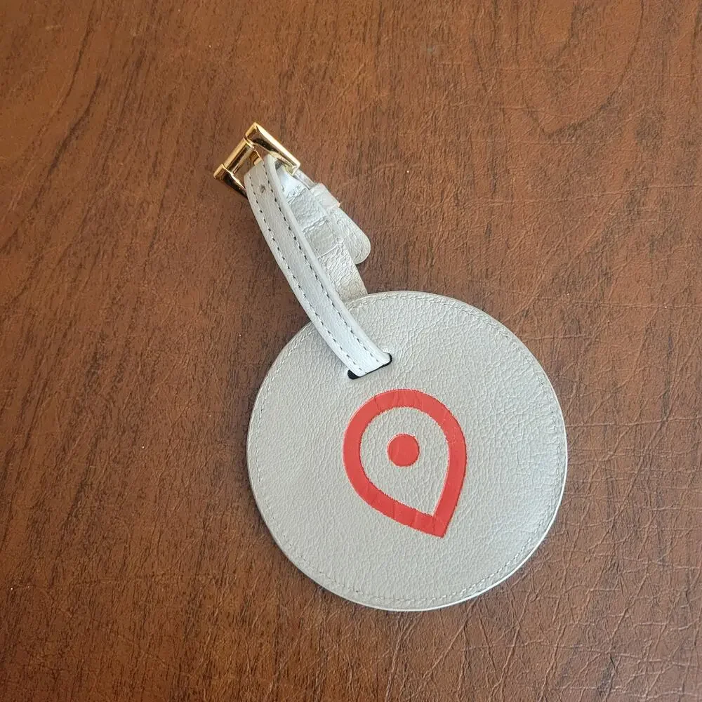 Round textured leather luggage tag in light grey with a red map